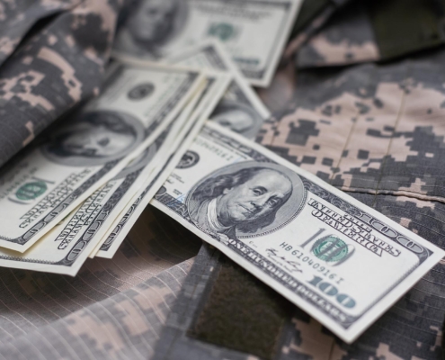 Image of money laying on top of a camouflage uniform.
